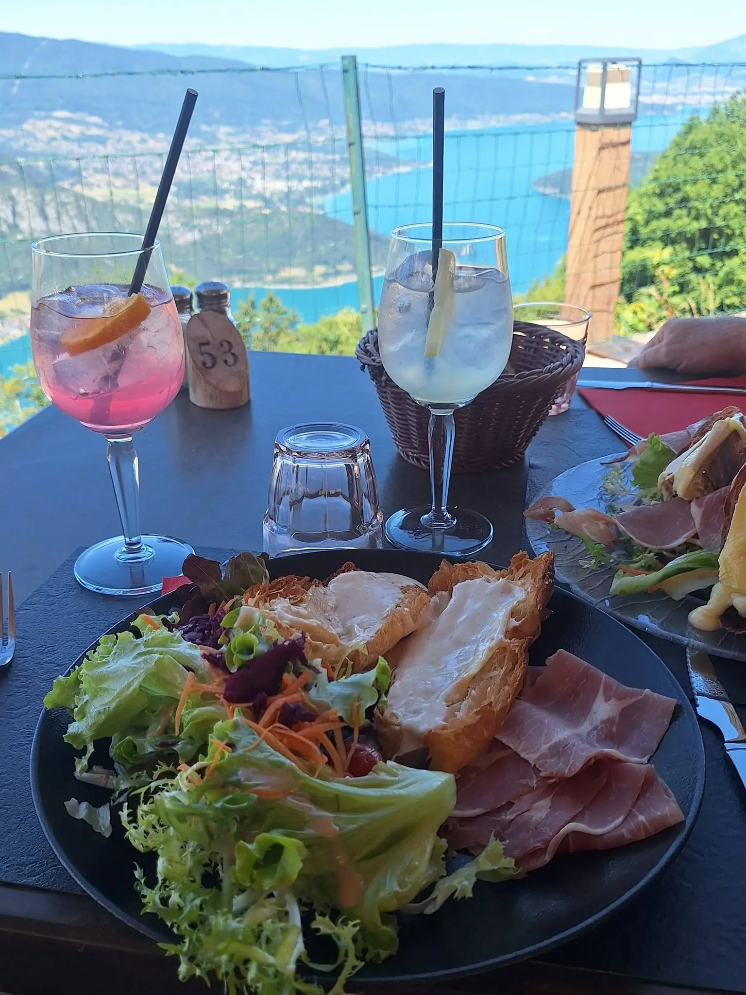 Apéritif en terrasse au Chalet La Pricaz, verres posés sur la table face au lac d’Annecy vu depuis le col de la Forclaz.