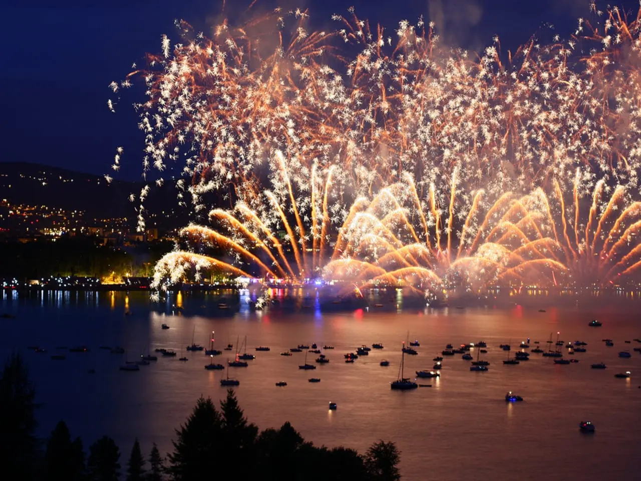 Le feu d'artifice de la Fête du lac au-dessus de la baie, vu d'une hauteur boisée, avec des dizaines de bateaux mouillés sur l'eau.