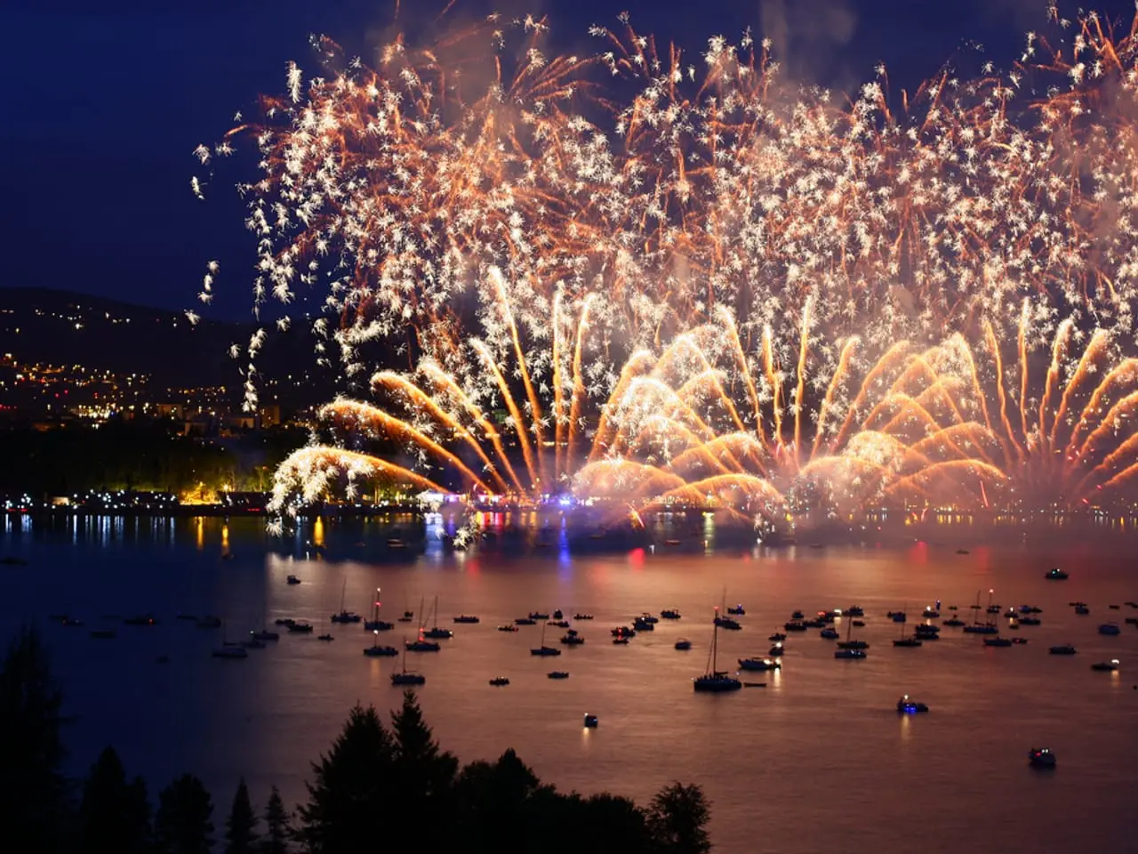 Le feu d'artifice de la Fête du lac au-dessus de la baie, vu d'une hauteur boisée, avec des dizaines de bateaux mouillés sur l'eau.