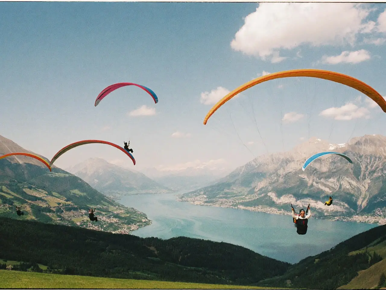 Quatre parapentes colorés au-dessus d’un lac de montagne, vus depuis un alpage.