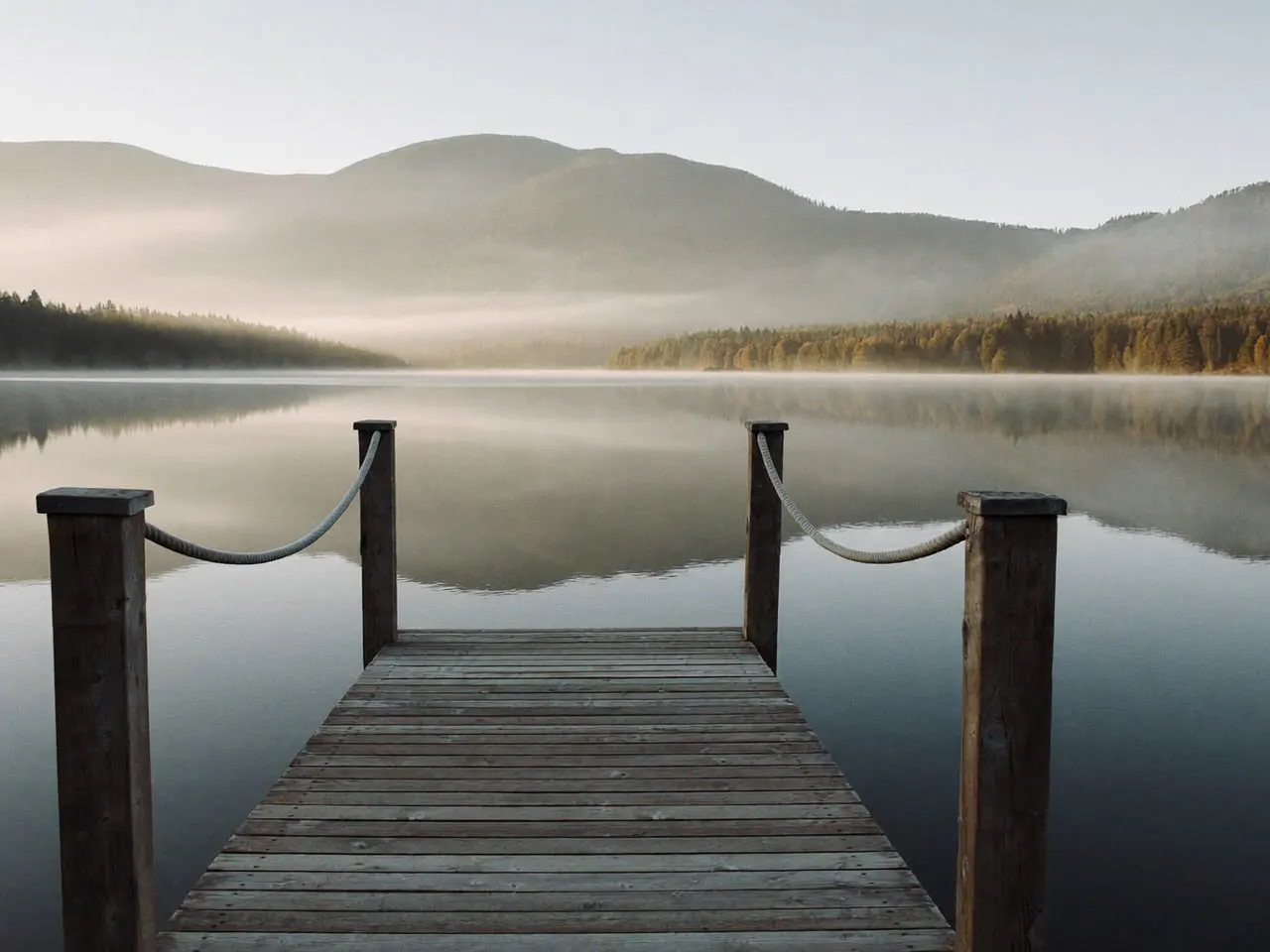 Ponton de bois avançant dans la brume au petit matin sur le lac d’Annecy, montagnes estompées à l’arrière-plan.